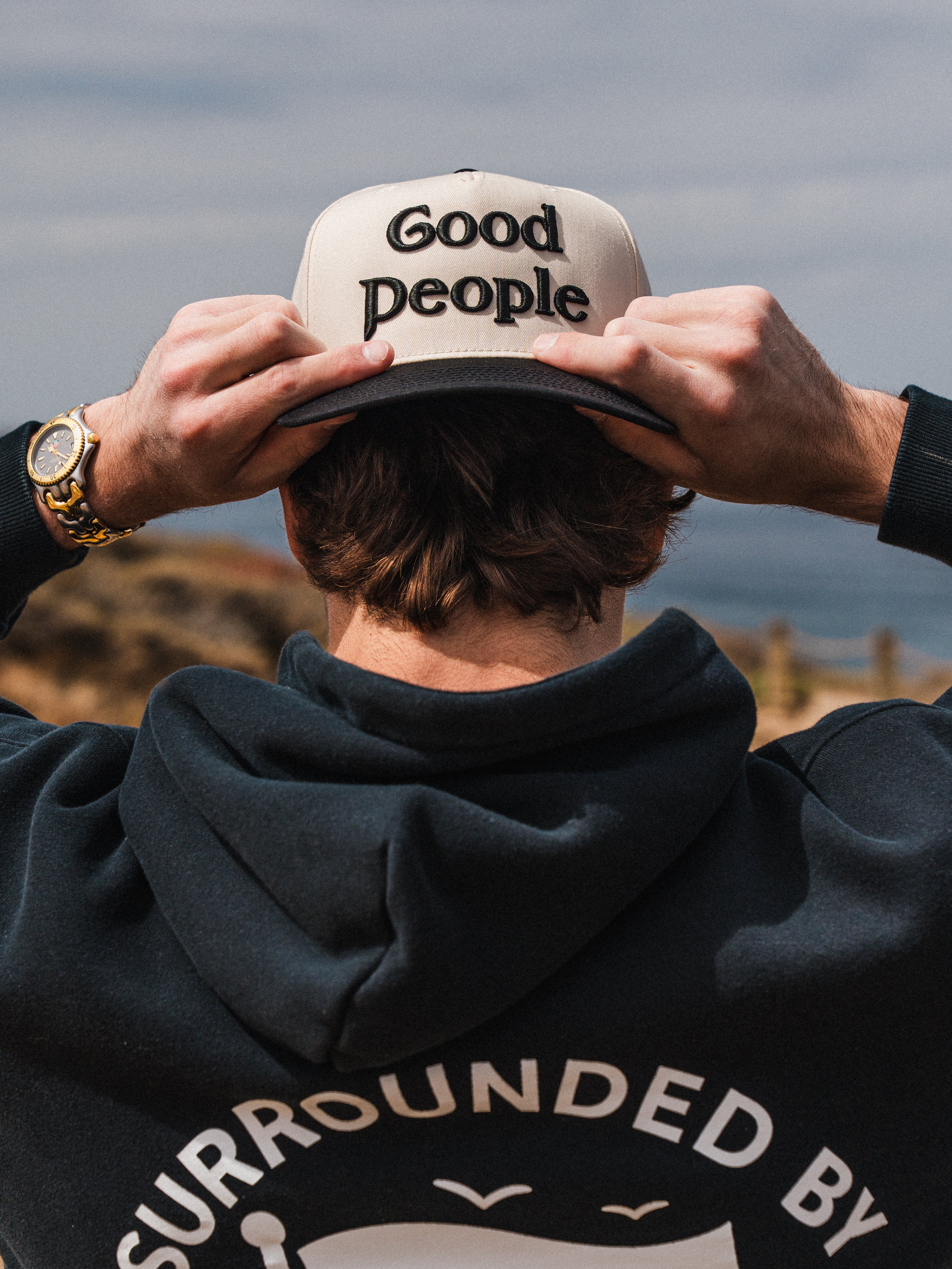 Good People Hat in black, being worn outdoors with a black surrounded by good people hoodie.